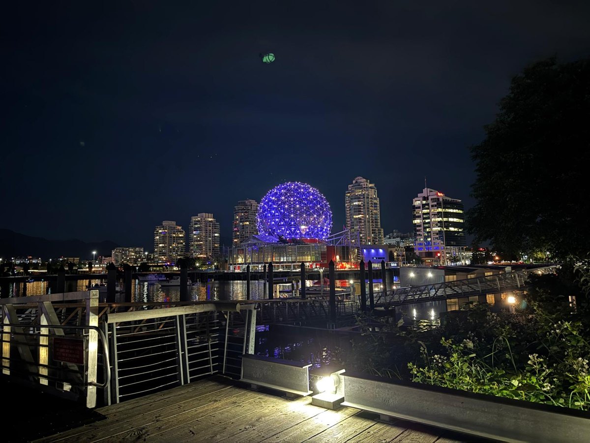 The lit sphere of Science World in Vancouver at night, a wooden boardwalk in the foreground – companion photo by Bernhard Houy
