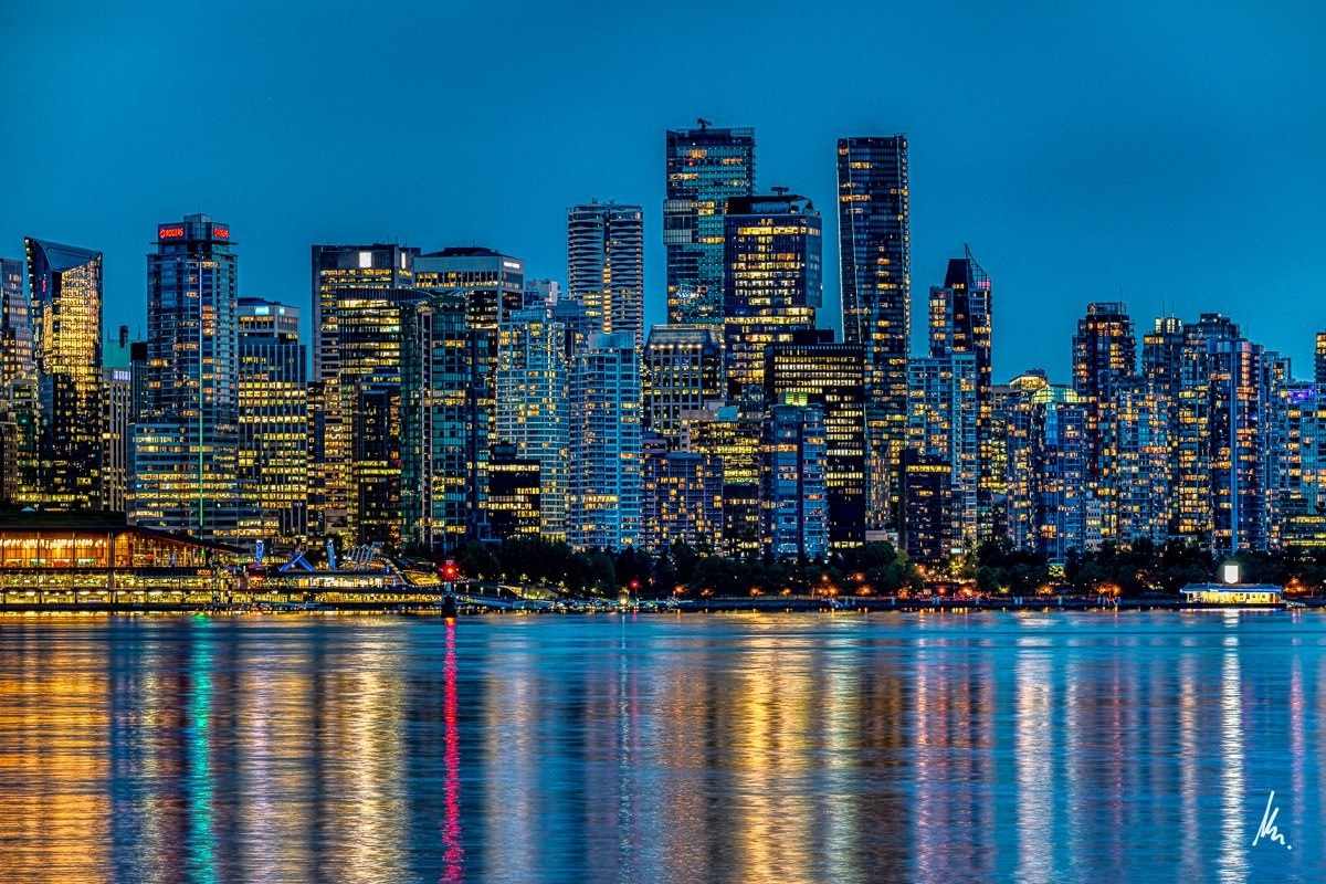 Vancouver skyline from Waterfront Park in North Vancouver in blue-grey twilight with golden lights and a small red dot in the water – photographic art by Bernhard Houy